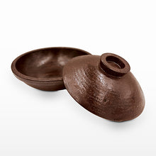 A dark brown textured ceramic bowl with its matching lid leaning against it, photographed on a clean white background.