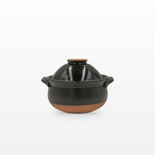 A small black glazed ceramic pot with a matching lid, featuring a natural terracotta-colored base and side handles, set against a plain white background.
