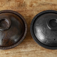 Two round dark brown wooden serving lids with textured rims, displayed side-by-side on a rustic wooden tabletop.
