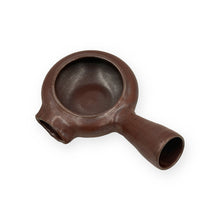 A dark brown ceramic tea scoop or whisk with a rounded bowl, a side pouring spout, and a handle, shown on a plain white background.